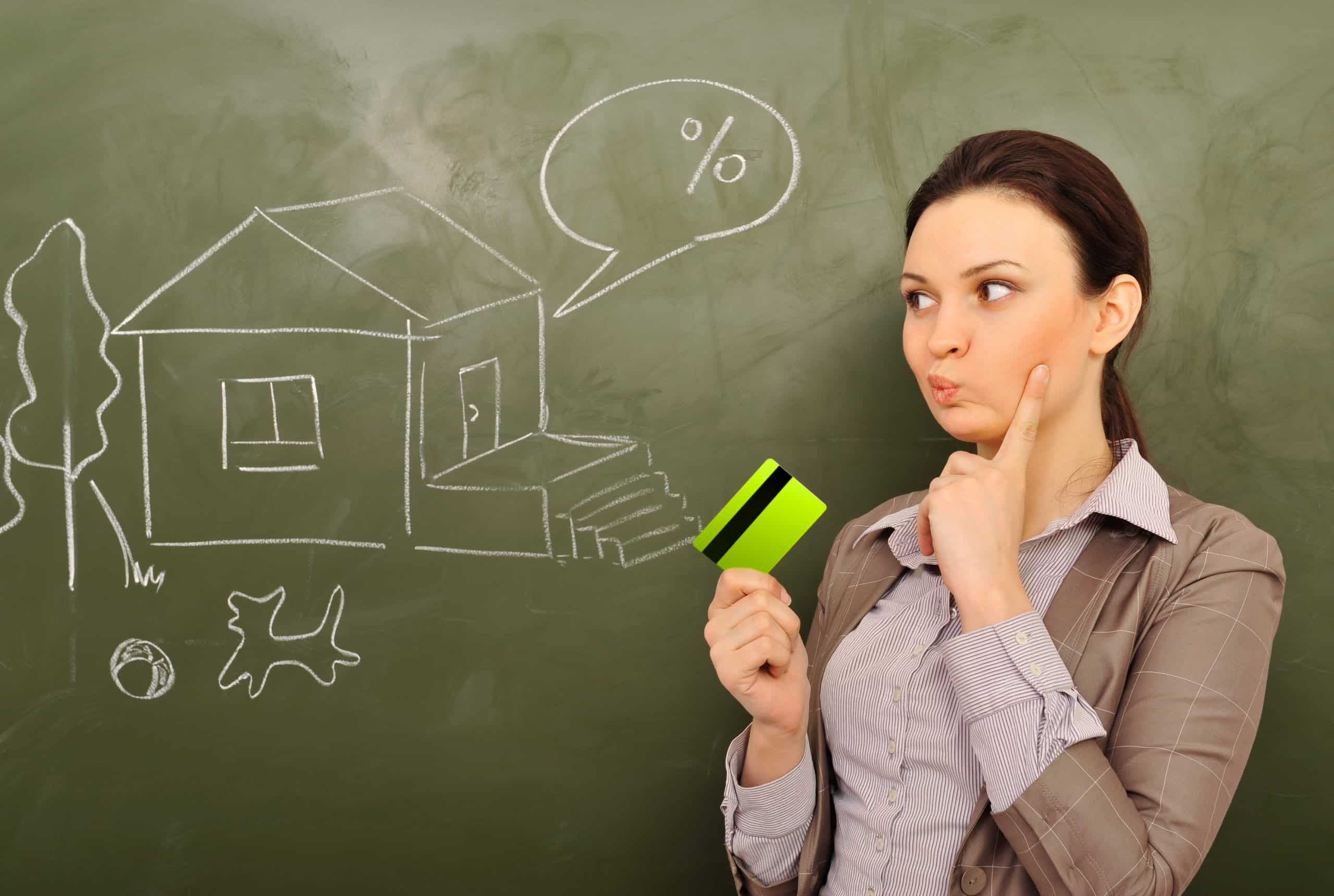 Closeup portrait of pretty young business woman against green board holding credit card and drawing beautiful house with backyard. Mortgage concept