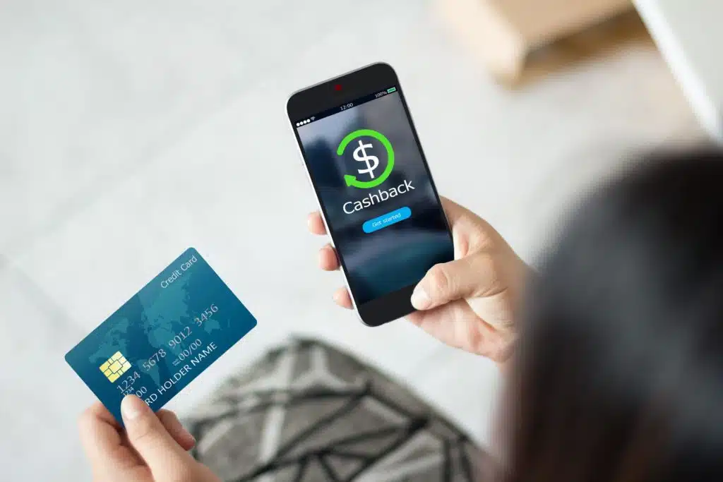 overhead shot of a woman holding a smartphone thats open to a cash back app, with a credit card in her left hand. 