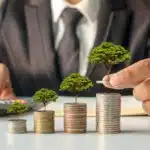 man in a suit sitting at a table counting his money and watching it grow