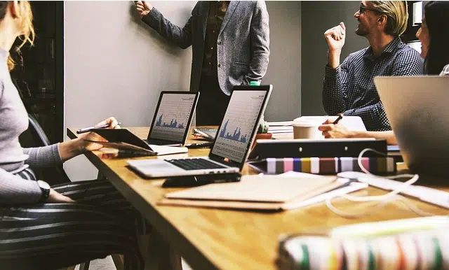 people in a meeting sitting around a conference table with laptops open on top