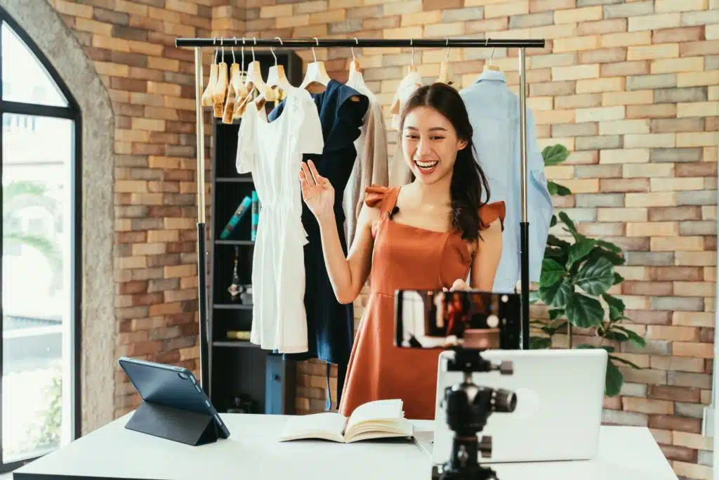 young woman filming a video with a clothes rack behind her