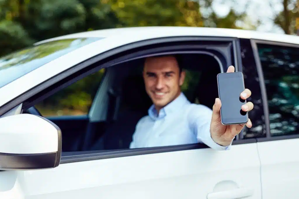 ride share driver holding a cell phone out of the window of his car